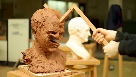 clay sculptor destroying his own work, destroying a clay bust with a stick for a second time