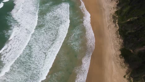 scenery of foamy waves moving towards sandy seashore of sawtell beach during summertime in new south wales, australia