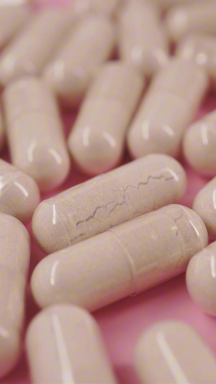 Primo piano di capsule bianche con polvere su sfondo rosa
