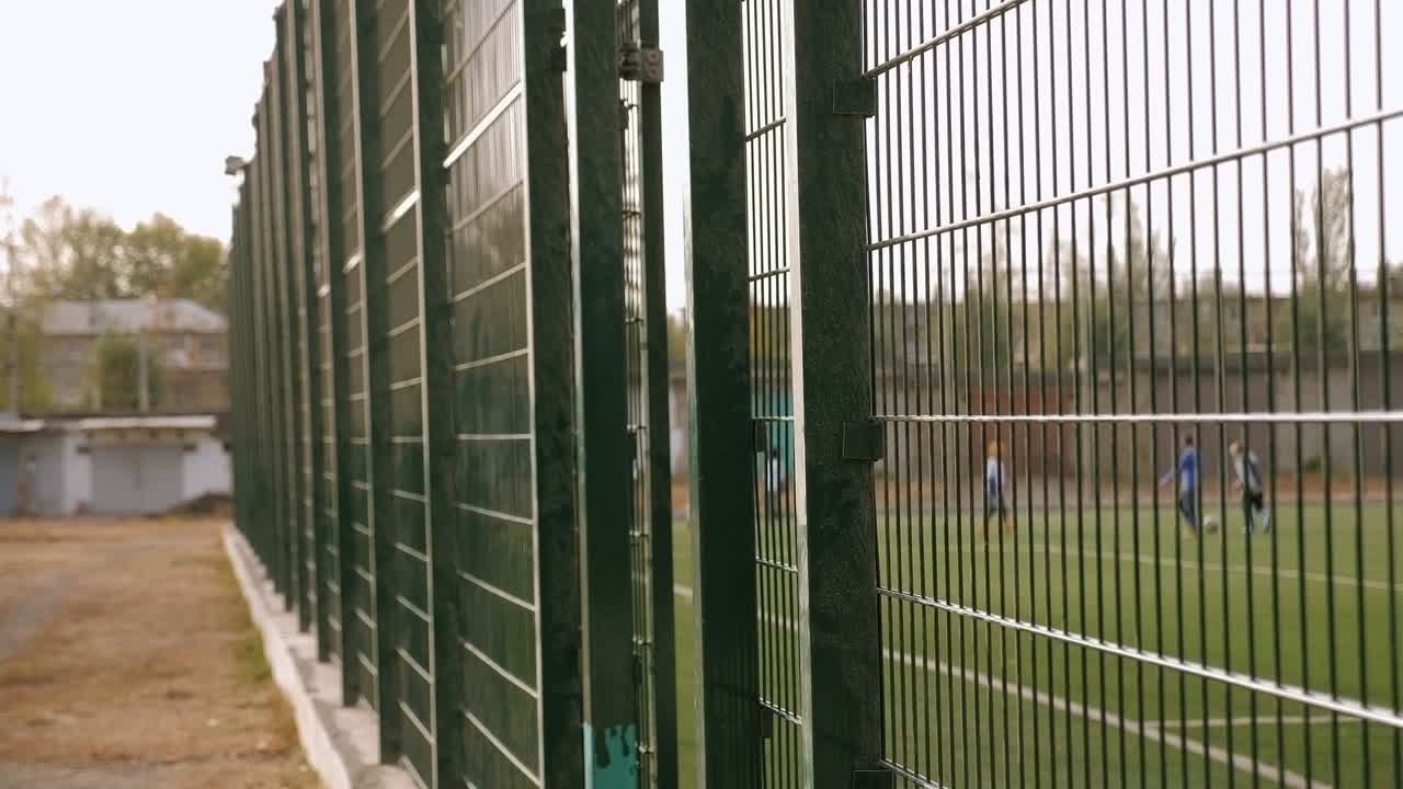 una valla de malla verde y polvorienta en un campo de fútbol artificial.