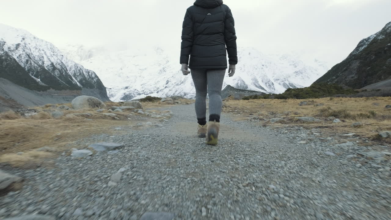 Inquadratura dinamica da dietro ad angolo basso di una donna che fa trekking tra montagne innevate in una fredda mattina d'inverno in Nuova Zelanda