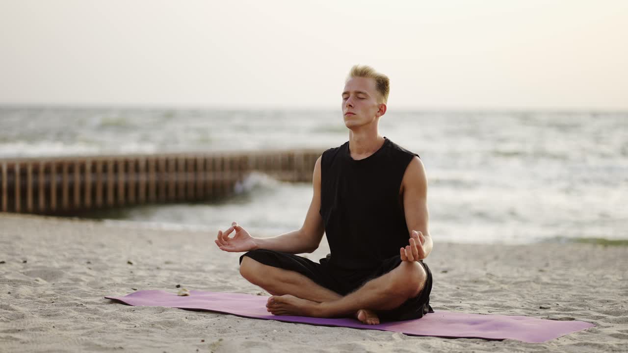 A young man is doing yoga and meditating on a sports mat while sitting during the dawn of the sun. Doing a specific exercise. Meditation, hands. Leisure time, recreation