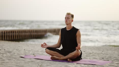 Un-Joven-Está-Haciendo-Yoga-Y-Meditando-En-Una-Alfombra-Deportiva-Mientras-Se-Sienta-Al-Amanecer-Del-Sol.-Haciendo-Un-Ejercicio-Específico.-Meditación,-Manos.-Tiempo-Libre,-Recreación