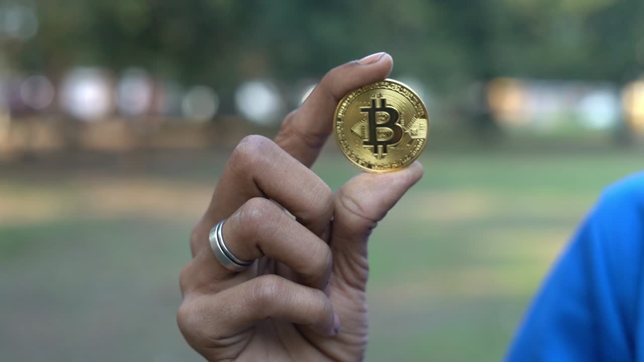 primer plano del oro de la criptomoneda bitcoin en manos de un niño asiático con camiseta azul