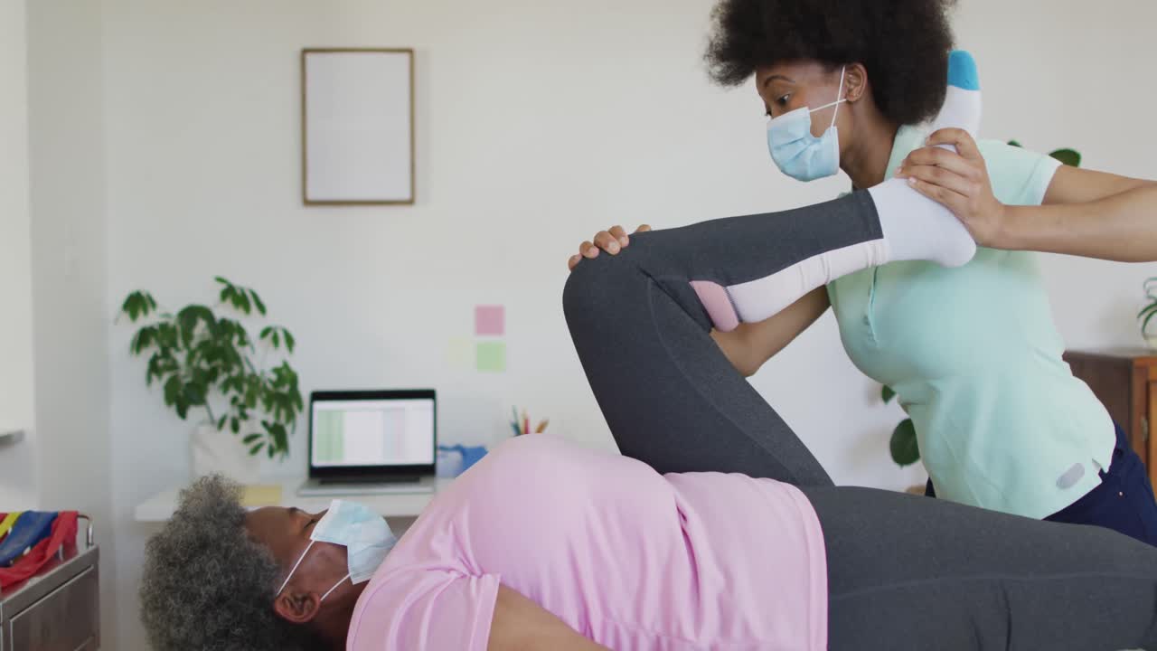 fisioterapeuta afroamericana feliz ayudando a una paciente anciana a hacer ejercicio en casa