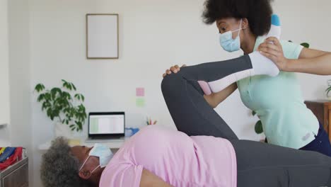happy african american female physiotherapist helping senior female patient exercise at home