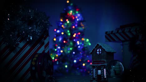 cámara ralentizando alejándose de un pequeño y lindo pueblo navideño cubierto de nieve como un gran, bien iluminado, hermoso árbol de navidad se sienta en el fondo, fuera de foco