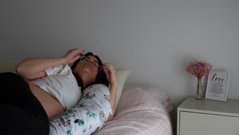 pregnant woman stretches in bed with glasses as morning light enters cozy bedroom