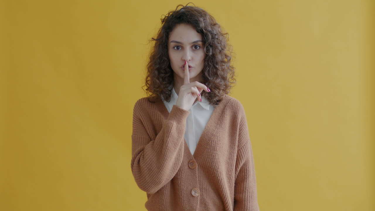 Mujer con el dedo en los labios frente a un fondo amarillo