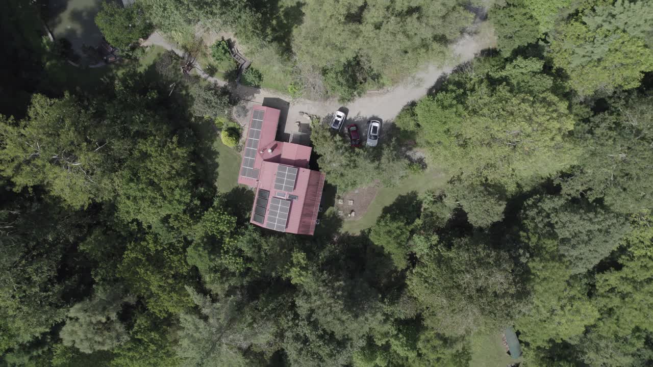 drone footage captures a picturesque bird's eye view of a charming red house nestled in the heart of a lush forest