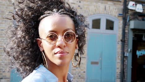 Fashionable-young-black-woman-wearing-blue-dress-and-sunglasses-looking-around-on-the-street,-side-view,-close-up