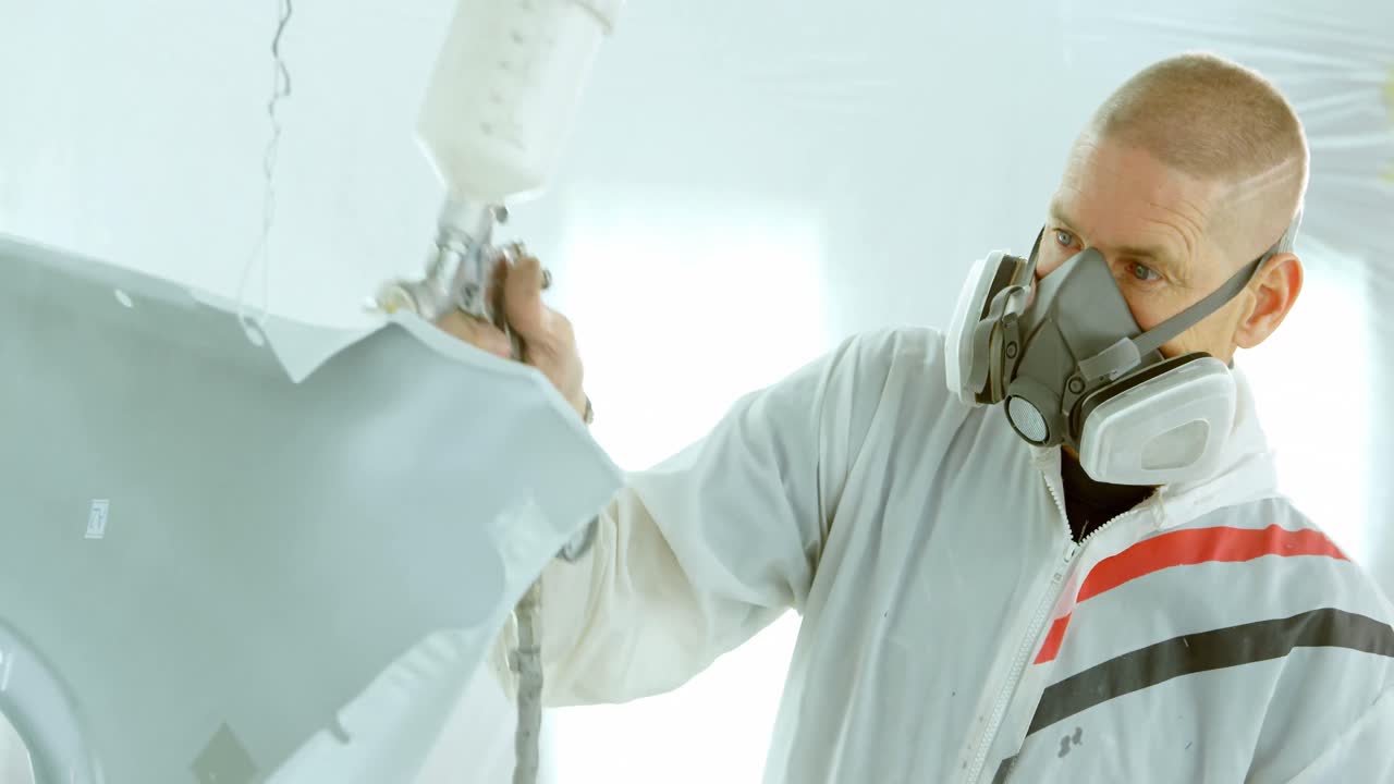 mecánico pintando piezas de automóviles con una pistola de pulverización eléctrica 4k