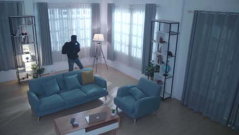 vista de cctv de un ladrón con una linterna robando una billetera, un teléfono inteligente y una computadora portátil en la casa de alguien antes de irse