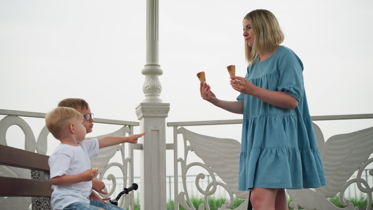 한 어머니 가 두 자녀 에게 아이스크림 코너 를 건네주는 모습 을 볼 수 있으며, 두 자녀 는 열렬 히 아이스크렘 코너 를 수집 하기 위해 손을 고 있다