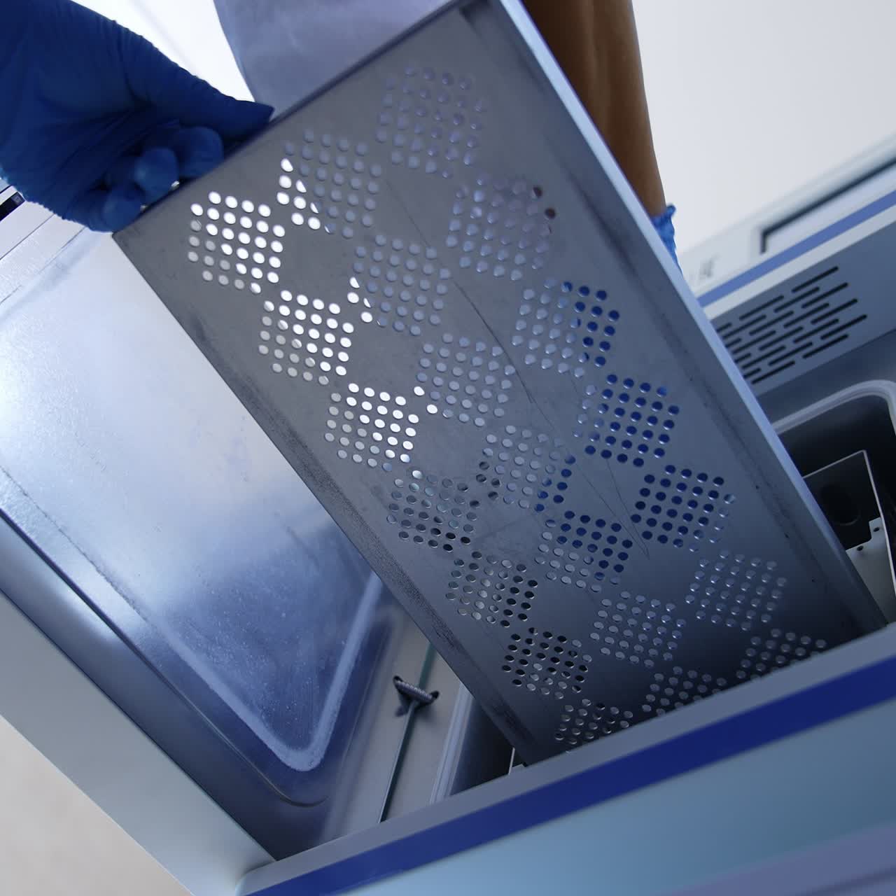 Gloved medic's hand open the door of apparatus and pulls the drawer. Nurse places the bag with tool into sterilizer machine. Low angle view