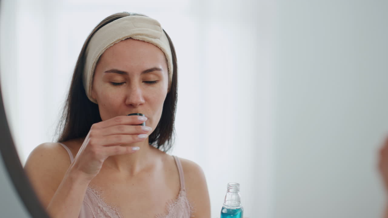Modelo feliz vertiendo enjuague bucal en el baño, primer plano. Señora sonriente enjuagándose la boca