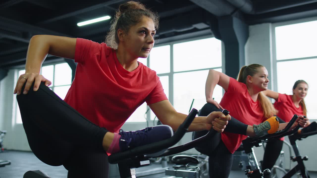 Group of smiling friends women class exercising training stretching on stationary bike at gym