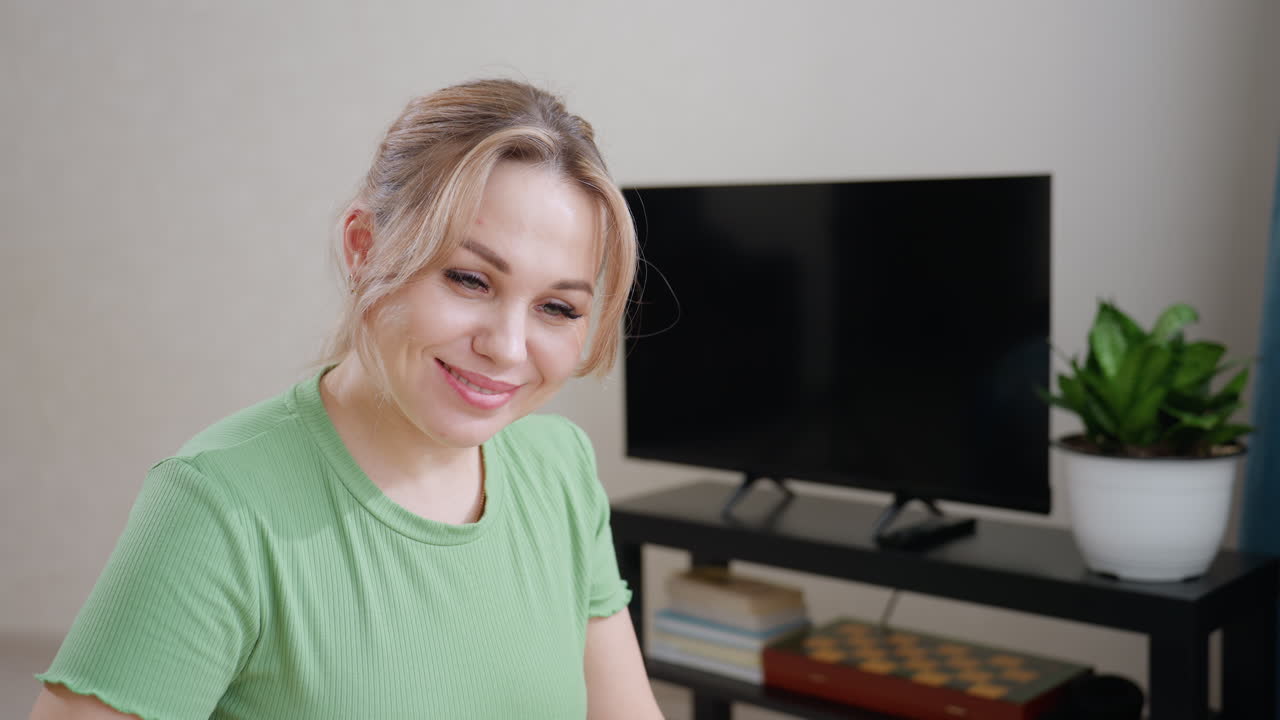 Young woman touches son gently on nose as he sleeps under blanket smiling warmly showing love care and affection in bright bedroom with television and plant in background
