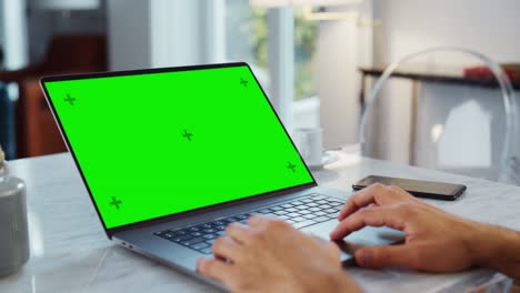 pantalla verde simulacro de pantalla en una computadora portátil. cerca de las manos de la persona trabajando desde el hogar moderno, usando el touch pad, desplazando el contenido. teléfono inteligente se encuentra al lado de la computadora.