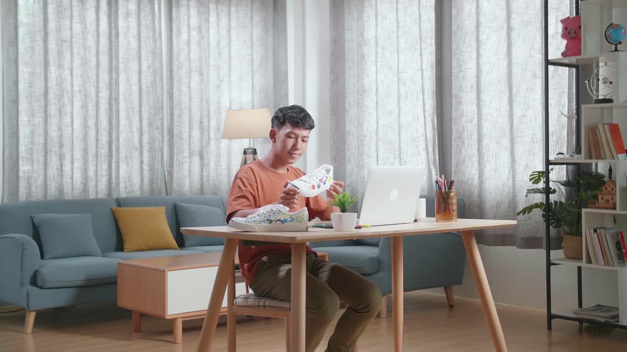 아시안 소년 신발 디자이너가 노트북을 들고 다채로운 패턴의 스니커를 보고 있습니다.