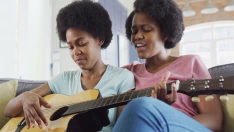 madre y hija afroamericanas felices sentadas en el sofá tocando la guitarra
