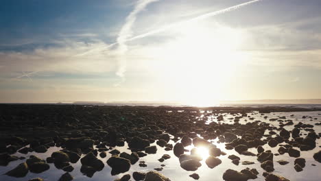 Most-amazing-breathtaking-cinematic-fly-over-low-tide-rocks-featuring-water-puddles-reflecting-sun-flares-at-sunrise's-golden-hour