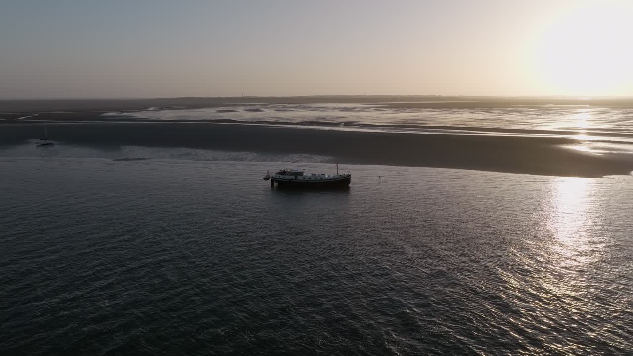 The drone circles around the Luxemotor boat stranded on the bottom of the Wadden Sea during the rising tide at dawn