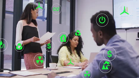 Green-energy-icons-animation-over-diverse-business-team-in-meeting-room