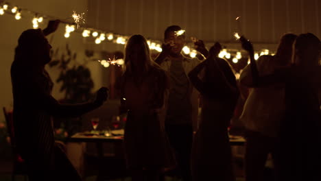 friends dancing on backyard. happy guys and girls holding sparklers in hands