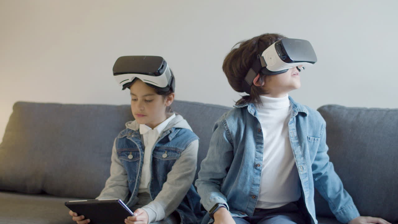 dos niños sentados en el sofá y probando gafas vr y tableta