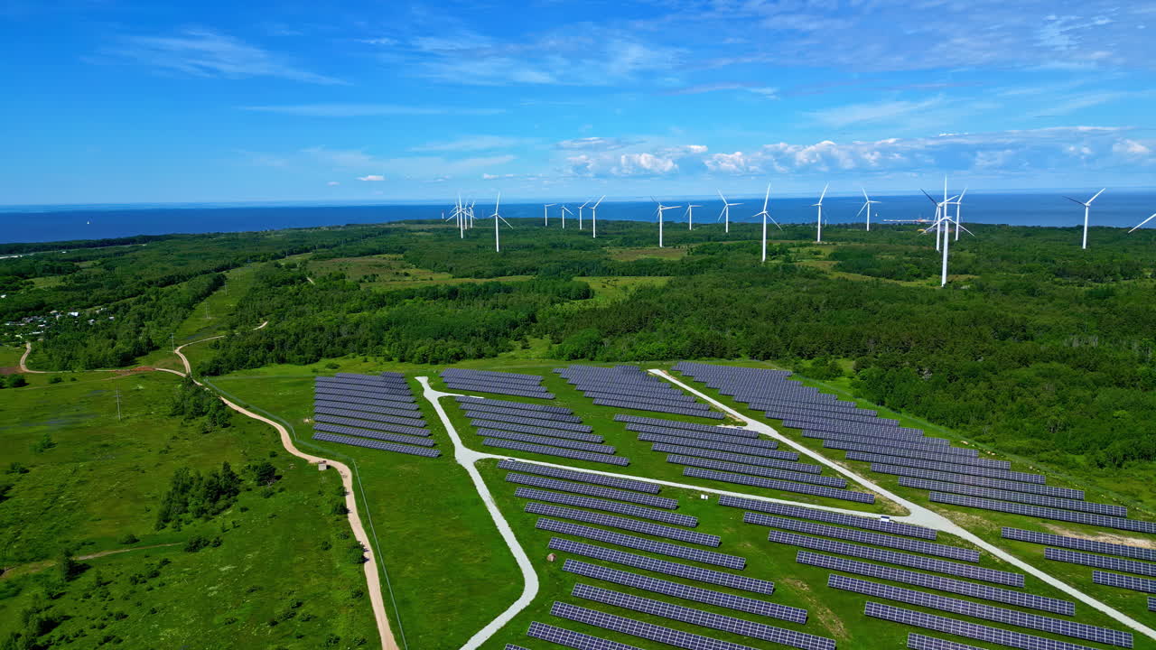 Aerial view of a large solar farm and wind turbines near the coast, showcasing renewable energy infrastructure.