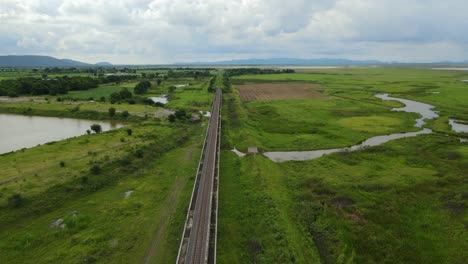 Imágenes-Aéreas-Hacia-Un-Horizonte-Escénico-Que-Revela-Un-Lago-A-La-Izquierda,-Humedales,-Tierras-De-Cultivo,-Ferrocarril-Elevado-Con-Un-Hermoso-Paisaje-Y-Lago,-En-Saraburi,-Tailandia