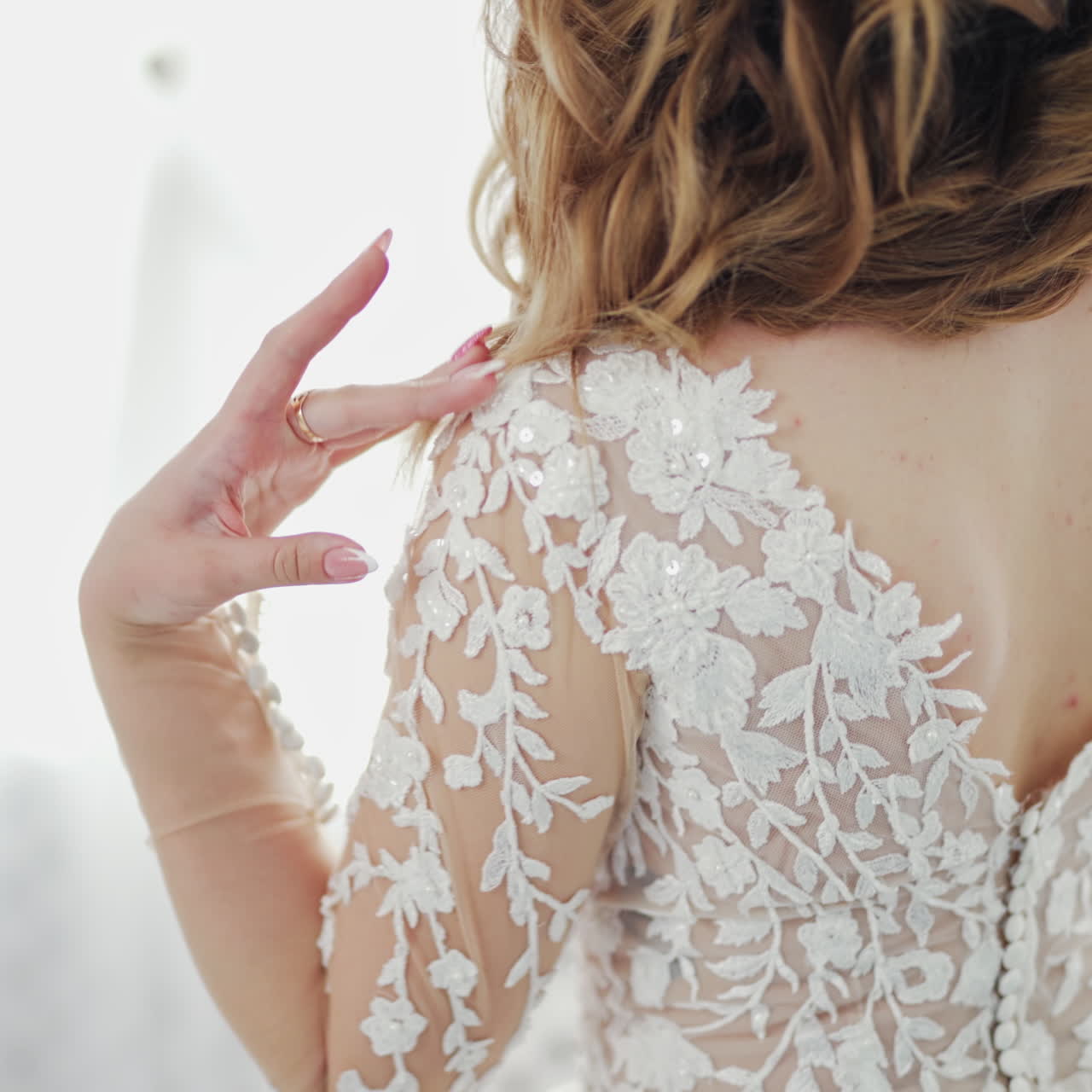 Young bride is dressed for the wedding. Back view of a beautiful, woman in white lace dress. Wedding dress details on attractive model indoors.