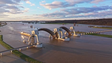 Aerial-orbit-drone-shot-at-the-weir-of-Driel-during-high-water-levels-with-the-doors-open-and-with-a-cargo-ship-passing-thru-the-weir