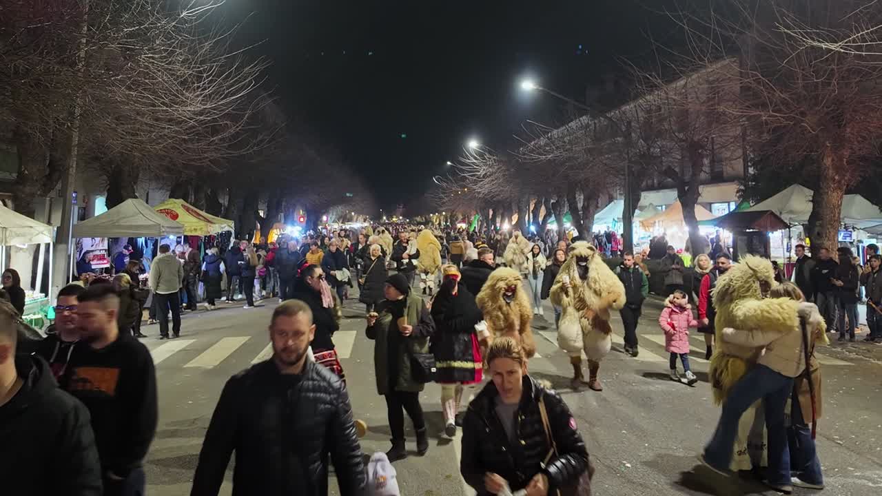 People stroll along the main street of Mohacs during the Busó-walking festival between the illuminated market stalls and locals dressed in animal skins during the evening.