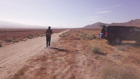 young man prepares to launch a consumer drone on sandy desert road path