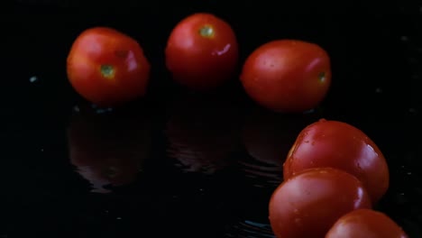 tomates de cereza rodando en un charco de agua negra y volando hacia arriba fuera del marco