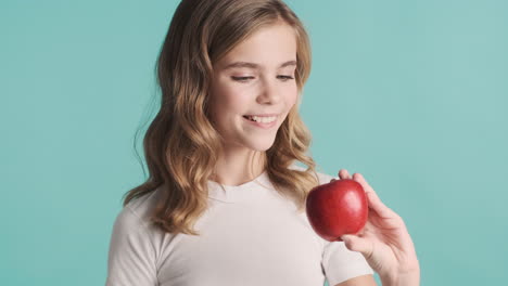 teenage caucasian girl in pijamas holding an apple in her hand and smiling.