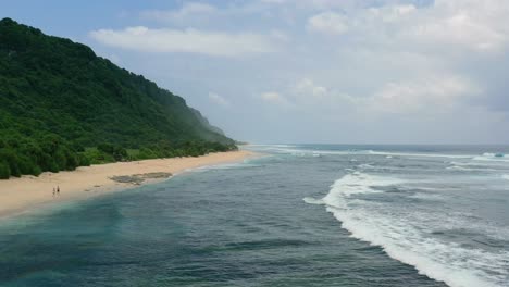 couple on empty white sand beach coastline in uluwatu bali on sunny day, aerial