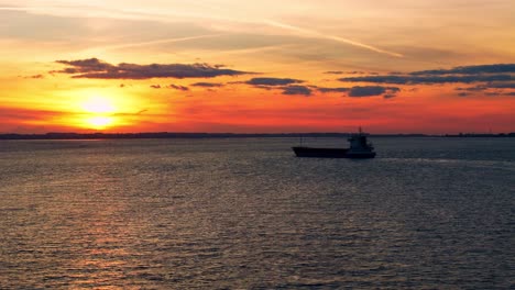 A-magical-moment-as-a-barge-boat-lazily-passes-under-the-Humber-Bridge-at-sunset,-immortalized-in-this-breathtaking-aerial-drone-footage,-where-the-river-gleams-in-the-sun's-golden-kiss