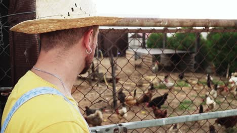 Young-caucasian-farmer-man-proudly-looking-to-his-hens-inside-chicken-run