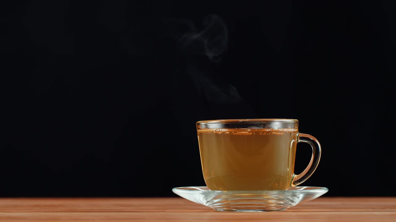 A steaming cup of hot tea on a wooden table with a black background