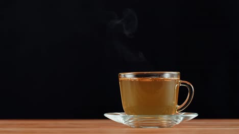 a steaming cup of hot tea on a wooden table with a black background