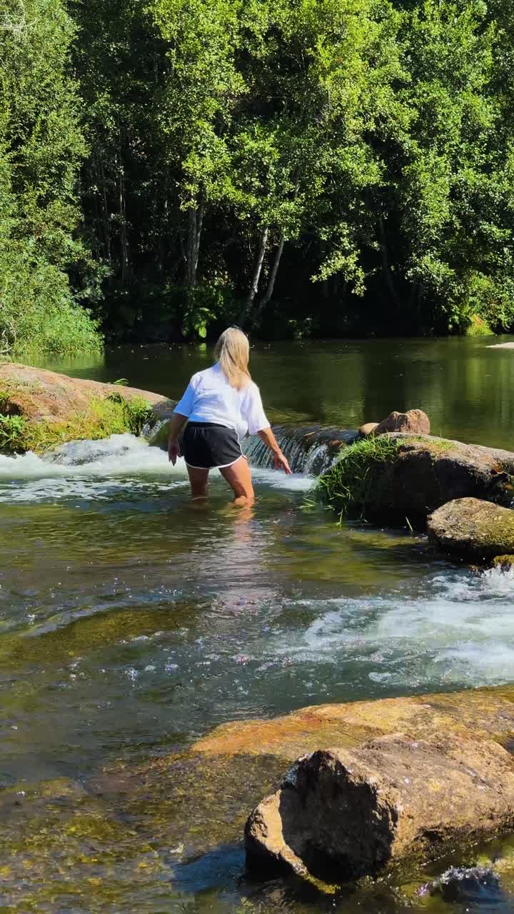 A woman tries to cross a fast flowing river between the rocks at a small waterfall
