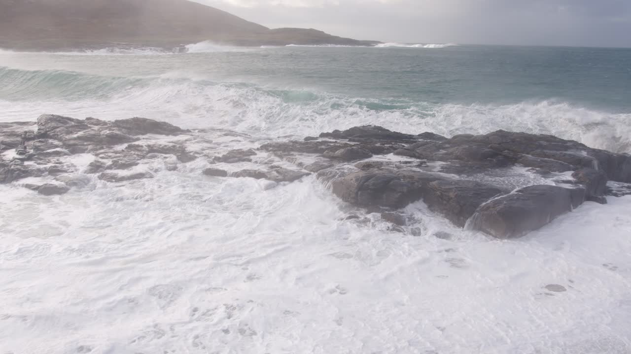 Ripresa panoramica al rallentatore di una grande onda bianca che si infrange sulle rocce durante una tempesta nella baia, vicino alla spiaggia di Tangasdale, nei pressi di Castlebay sull'isola di Barra.