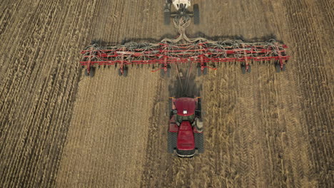 tractor pulling seeding equipment on field revealed lake scenery in saskatchewan, canada