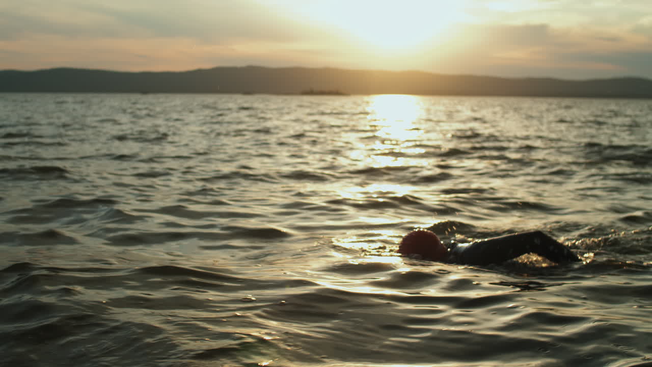 해가 지면 호수 에서 수영 하는 여자 트라이애슬레트 선수