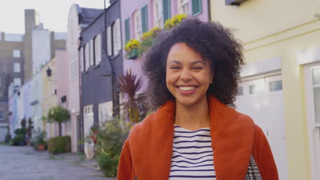 Portrait-of-smiling-woman-wearing-coat-standing-on-cobbled-mews-street-on-visit-to-city-in-autumn-or-winter---shot-in-slow-motion