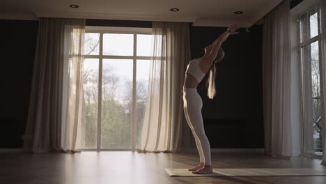 a young woman in a white suit in a gym trains yoga in the sun in slow motion