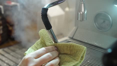 professional female barista cleans steam wand with cloth